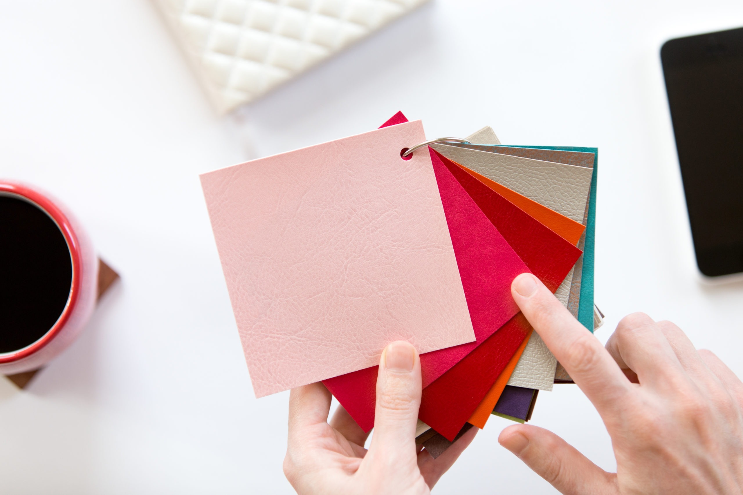 Female hands choosing a color fabric pattern above a white office desk. Top view with copy space, design concept photo Le Décor de Jules - Conseil en aménagement & décoration intérieure - nuancier matière